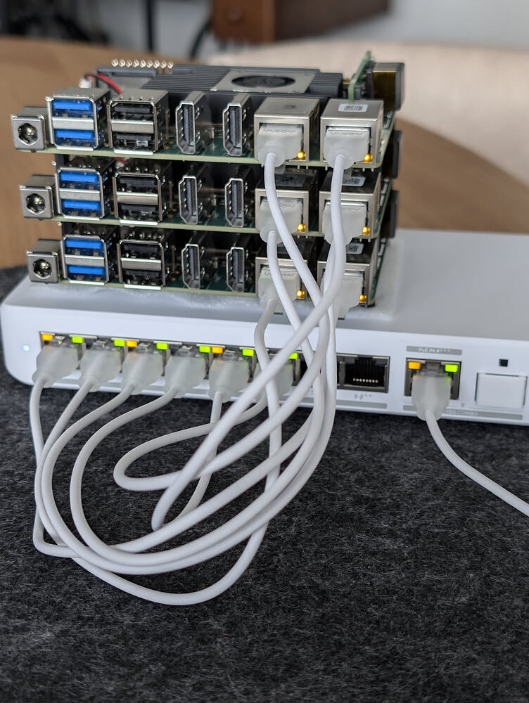 Three Radxa Rock 5T boards stacked above a Ubiquiti Flex 2.5G PoE switch with short white network cables connected.